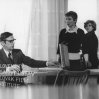  
Za stolom sedí s okuliarmi na očiach Ivan Mistrík (Charvát), vpravo stojí Daniela Kolářová (Zuza Melichová) a pri okne stojí Viera Strnisková (učiteľka)