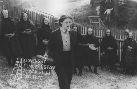 Milka Zimková (Vavjaková) zdroj: skcinema.sk 
V popredí kráča Milka Zimková (Marka Vavjaková), v pozadí stoja v rade dedinské babky